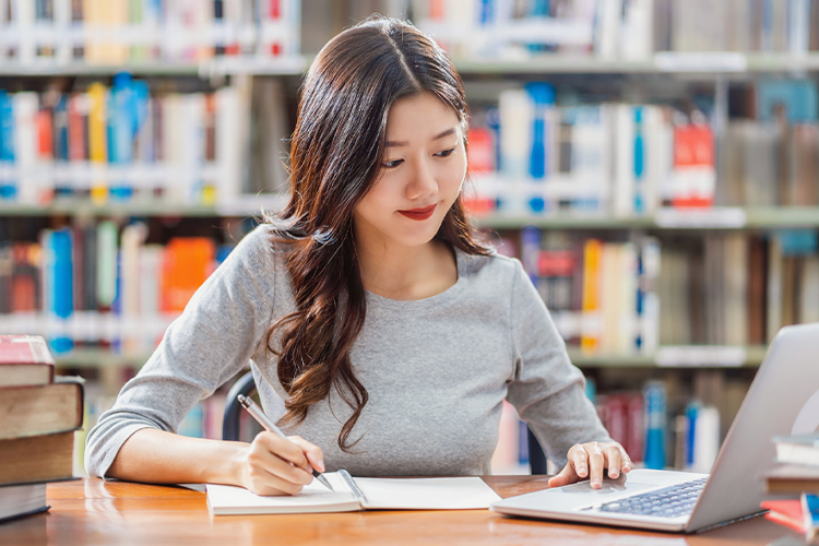 Woman writing in her notebook while using a laptop